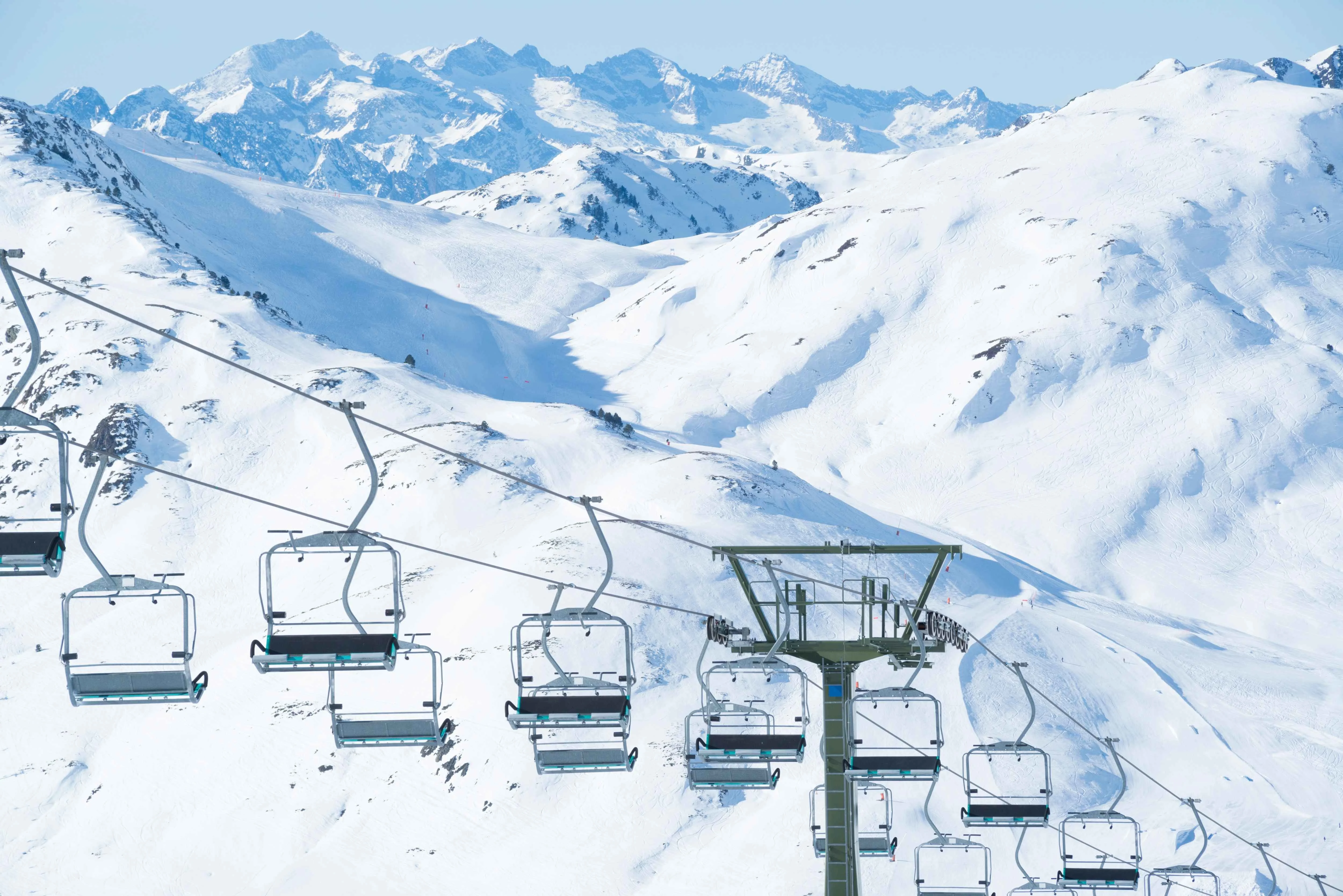 Empty ski lifts glide above a pristine alpine landscape, revealing wide open slopes and snow-dusted ridges framed by jagged peaks in the distance