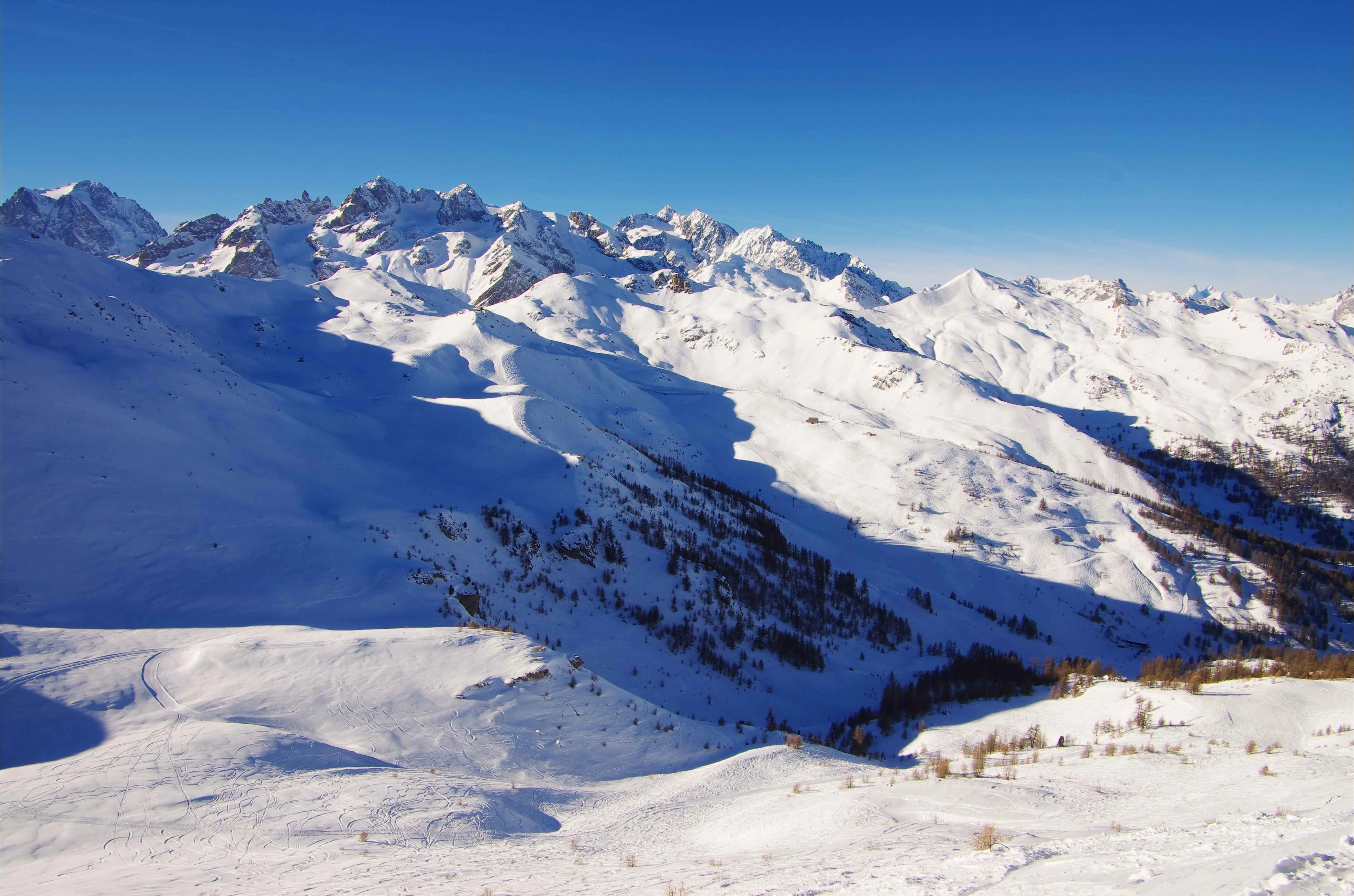 An expansive view over Serre Chevalier reveals pristine, untouched powder fields and dramatic Alpine peaks under a vivid blue sky, capturing the quiet beauty of the southern French Alps