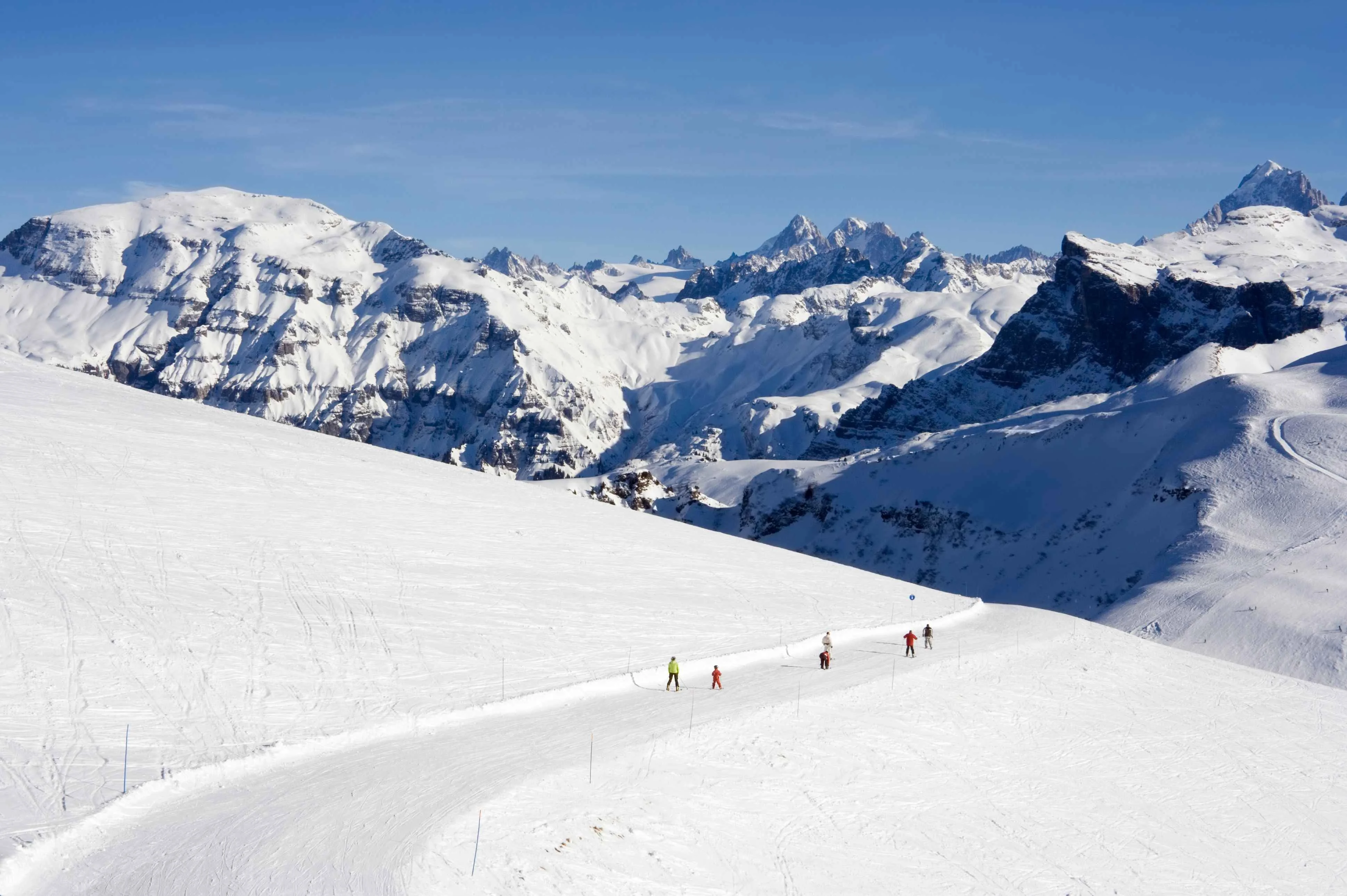 A gentle slope winds through the snow-covered peaks of Samoëns, where skiers make their way beneath a backdrop of rugged Alpine summits and deep blue skies, perfectly capturing the resort’s serene beauty.