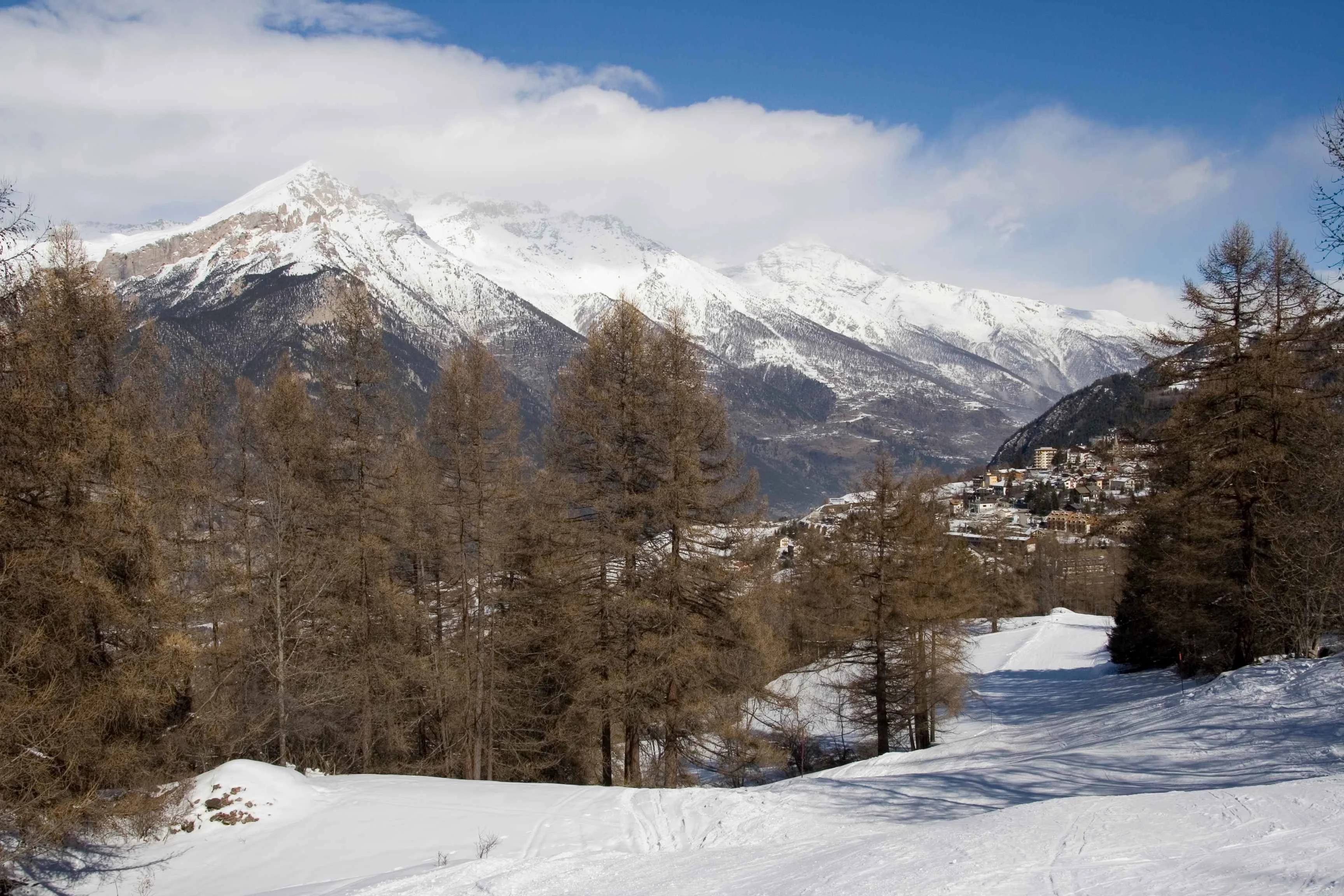 A snowy trail winds through alpine forest above Sauze d’Oulx, revealing panoramic views of the snow-dusted rooftops and the dramatic peaks of the Italian Alps beyond blending nature, village charm, and mountain adventure