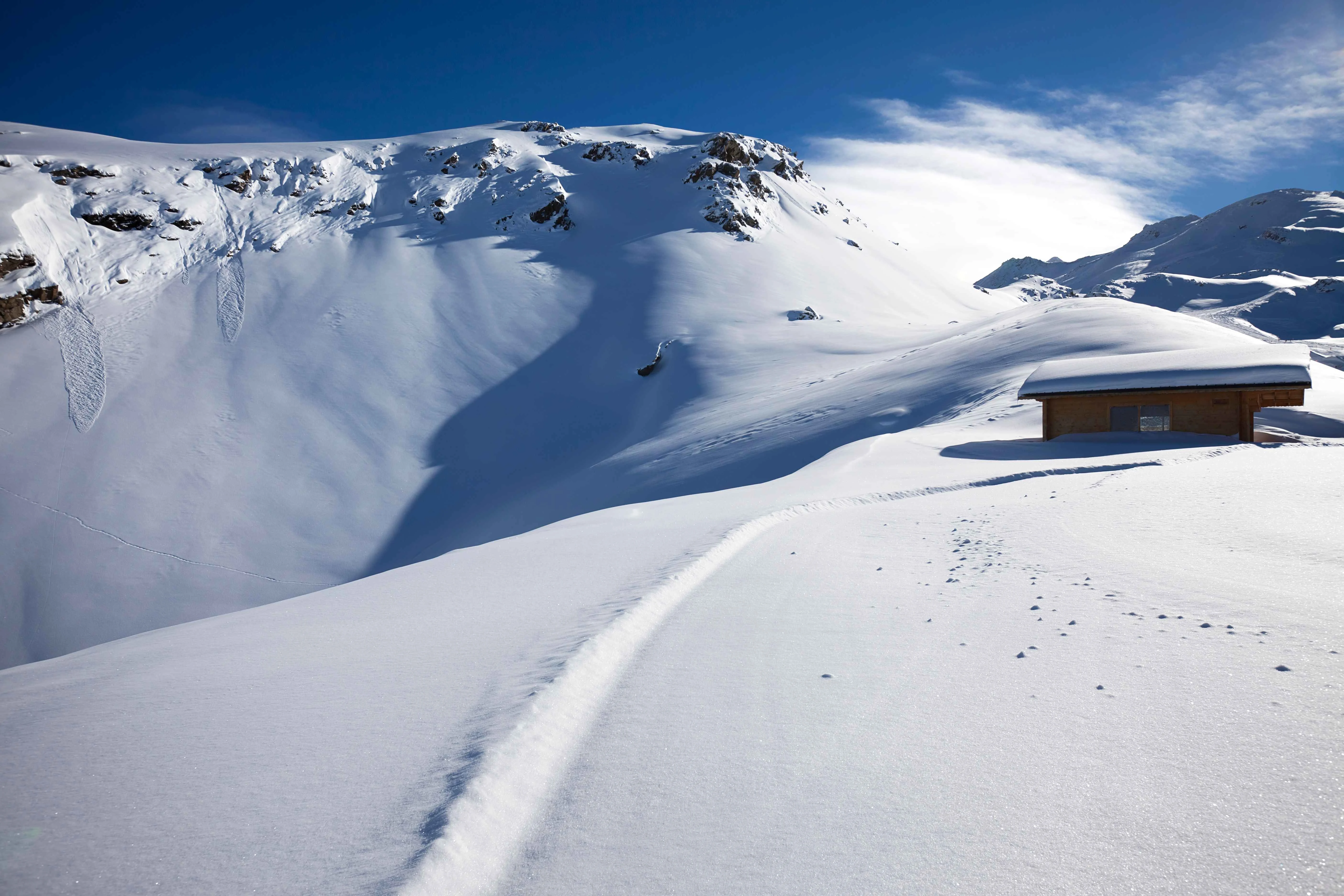 Snow-covered mountain landscape in the French Alps with a wooden cabin under a clear blue sky