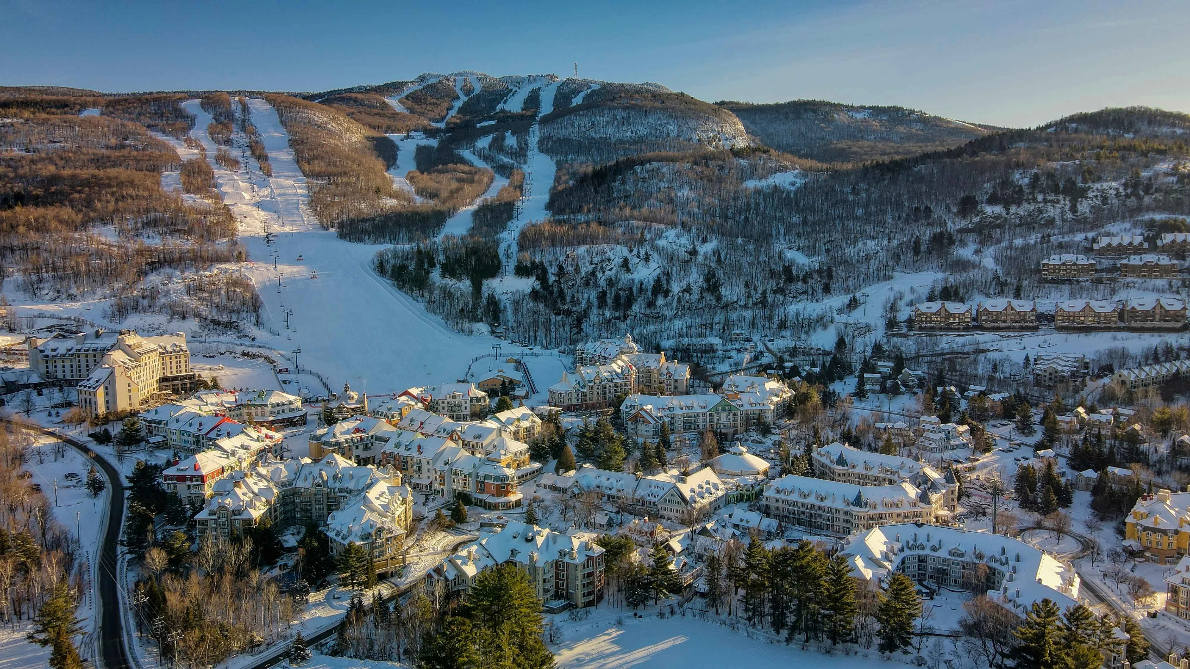 Aerial view of a snow covered ski resort village with ski slopes and chairlifts on a forested mountain