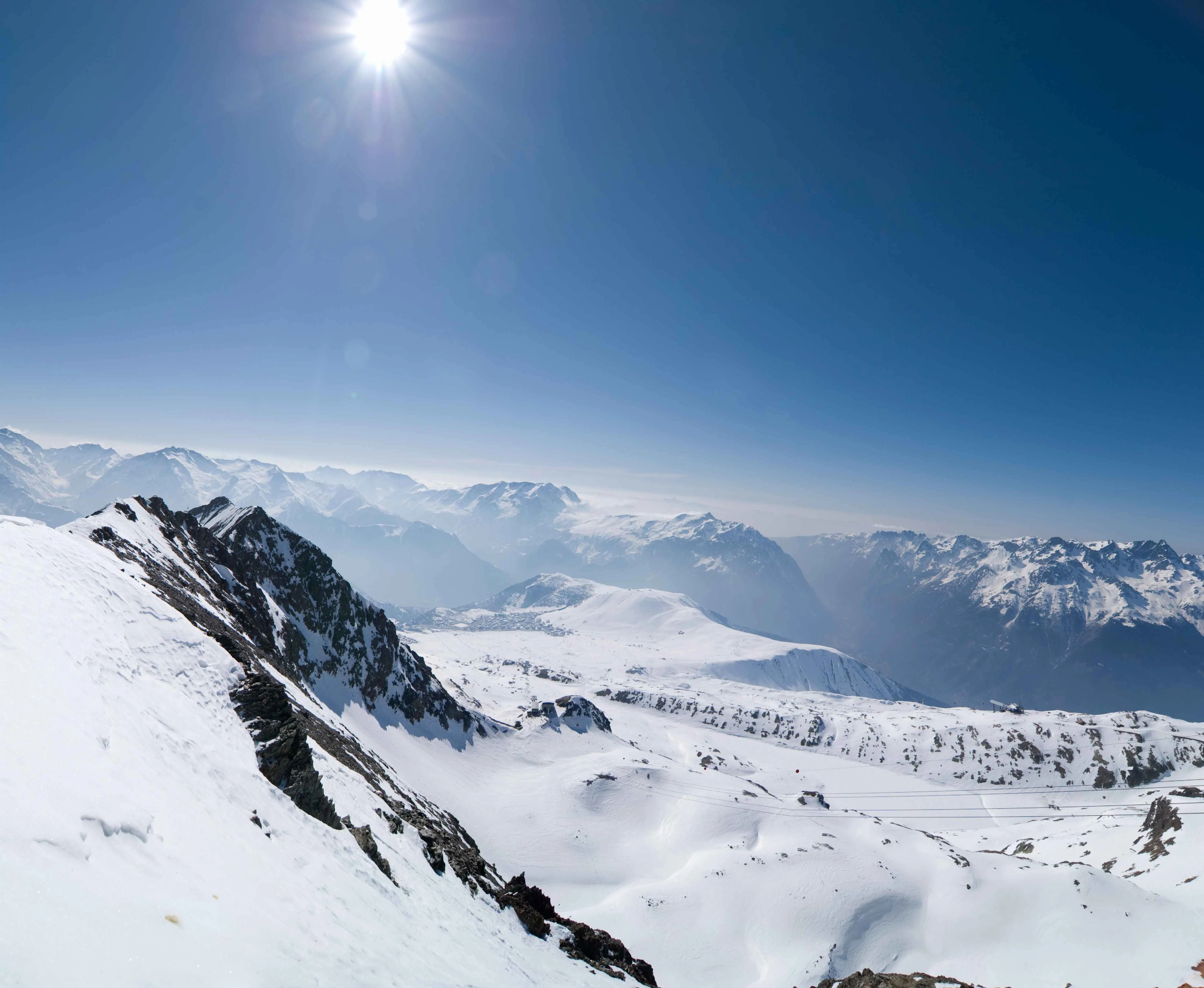 Snow-covered mountain peaks under a bright sun and clear blue sky in Alpe d'Huez, French Alps