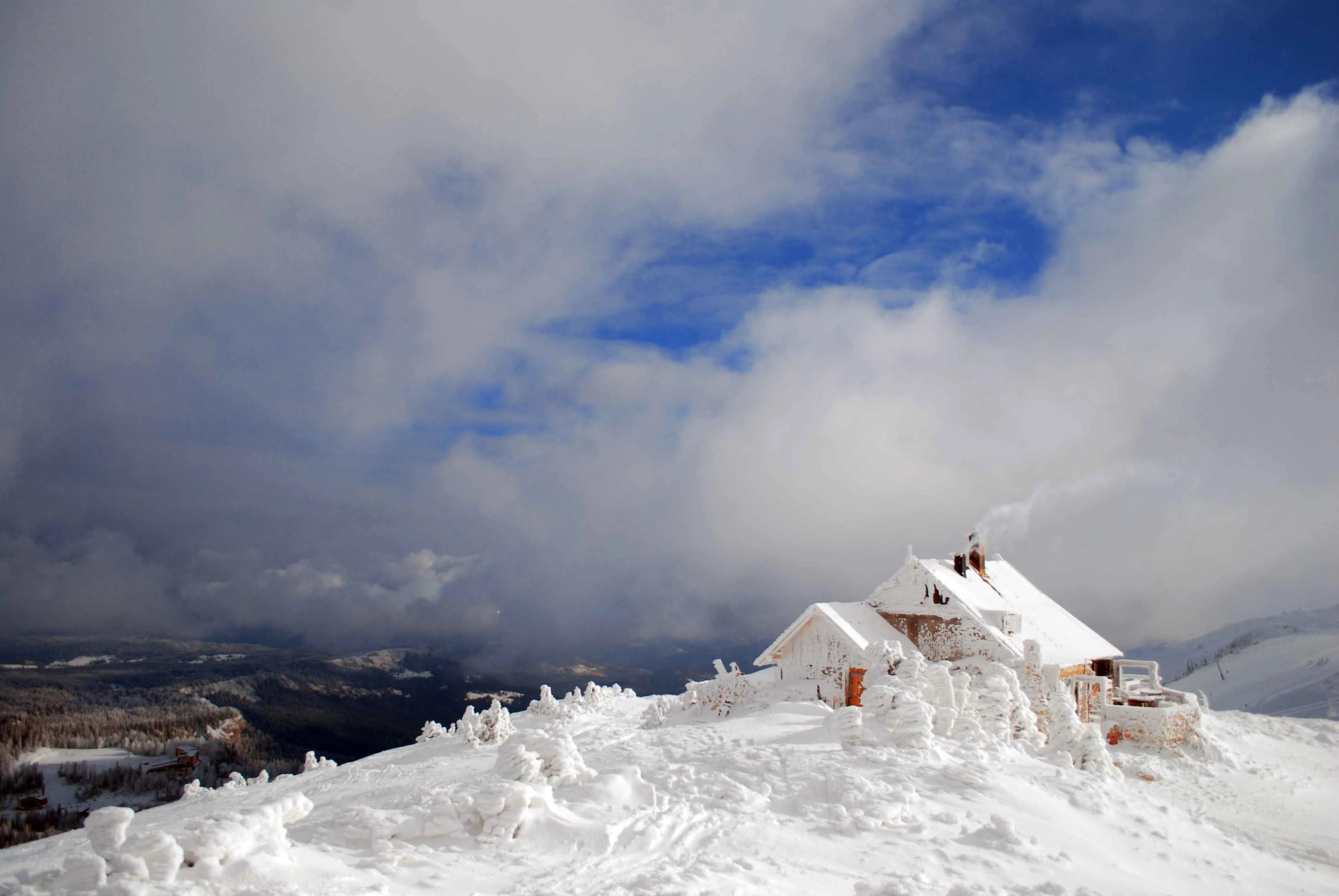 Snow-covered mountain cabin with smoke rising from the chimney under a dramatic cloudy sky in Jahorina, Bosnia and Herzegovina.