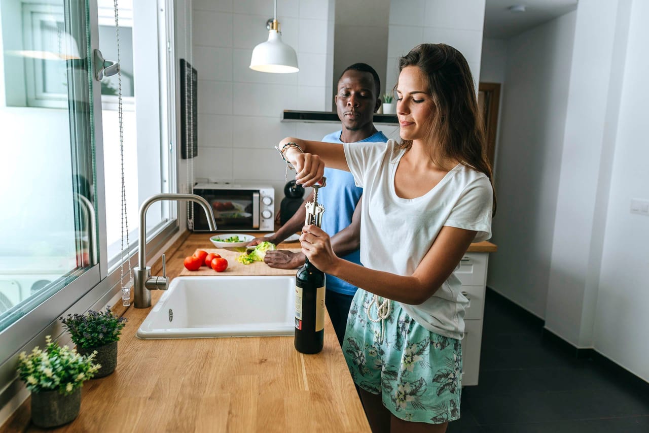 Woman opening bottle of wine next to man in kitchen
