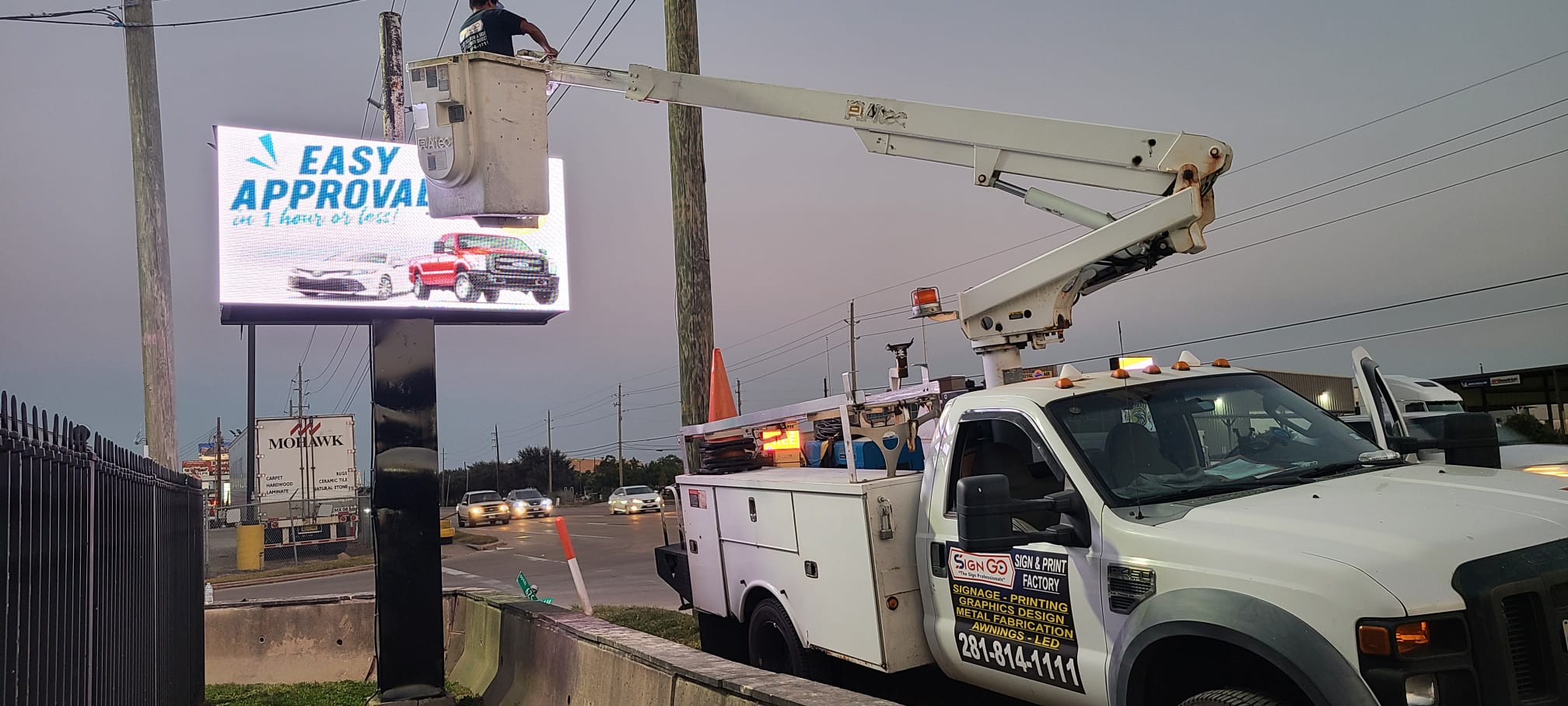 Technician programming a digital dealership message center from a boom truck