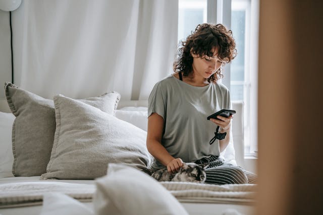 A young woman on her bed, focused on her smartphone