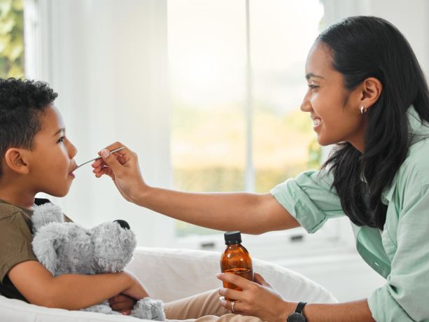 elinde şurup şişesi olan anne kaşıkla çocuğuna şurup içiriyor