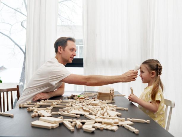 Bir baba kızının ateşini infrared termometre ile ölçüyor