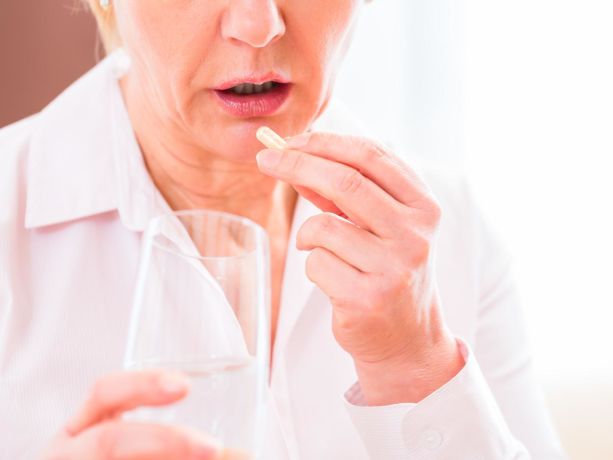  elinde bir bardak bir de hap olan bir kadın ilacın nasıl alınacağını gösteriyor