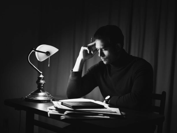 Karanlıkta lambası açık düşünen kitap okuyan genç bir adam