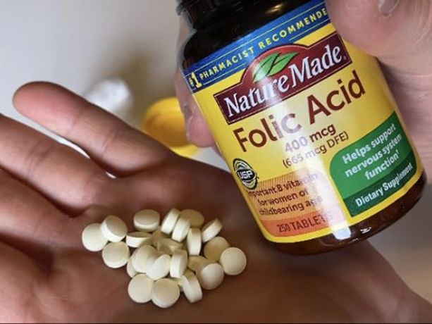 Nature Made Folik asit şişesi yanında bir el bu ilacın tabletlerini gösteriyor
