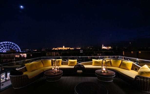 A lounge on the rooftop deck features yellow couches illuminated by the soft light of the port.