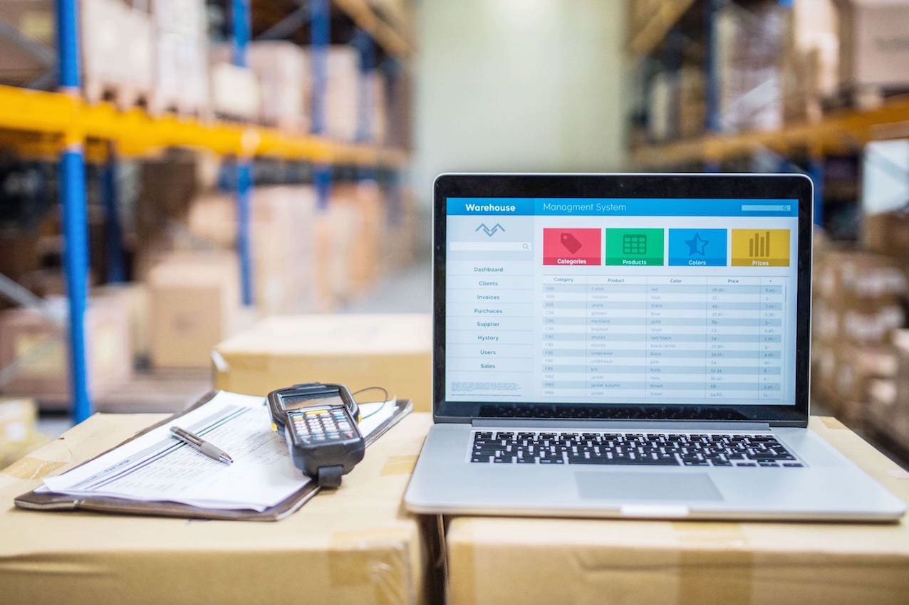 Dropshipping eingeschalteter PC neben einem Buch und Scanner auf einem Tisch vor einem DepotCity Dropshipping Lager