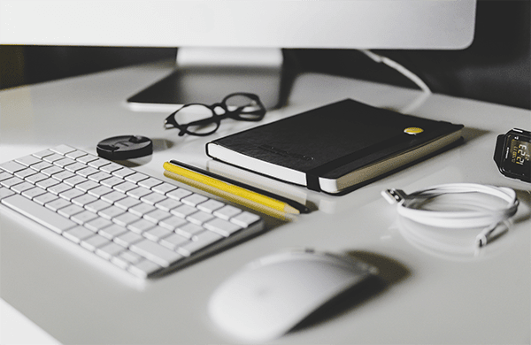 Photo d'un bureau avec un clavier, un carnet, des lunettes, une souris
