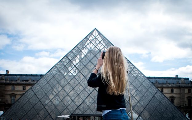 Discover the beauty of the Louvre Museum through the lens of a young girl, capturing its elegance with her camera in hand.