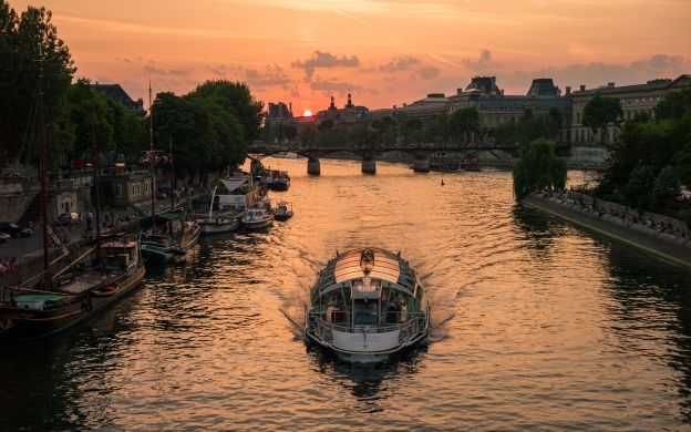 A stunning photograph of a cruise ship in the peaceful Seine River with the most beautiful sunset serving as the perfect background.