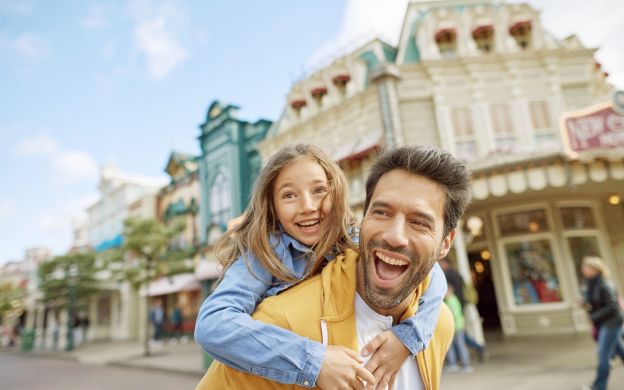 A joyful photograph of a father daughter duo in front of Disneyland Paris, excited to experience all the fun rides and attraction.
