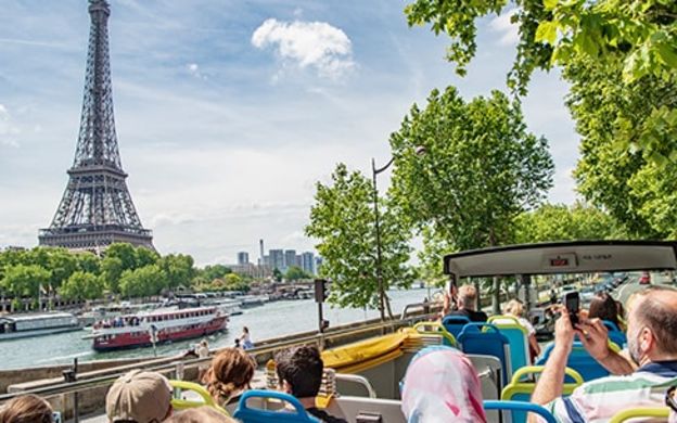 Sightseers enjoying the picturesque view of the Eiffel Tower and a cruise ship while taking photos from their comfortable bus seats.