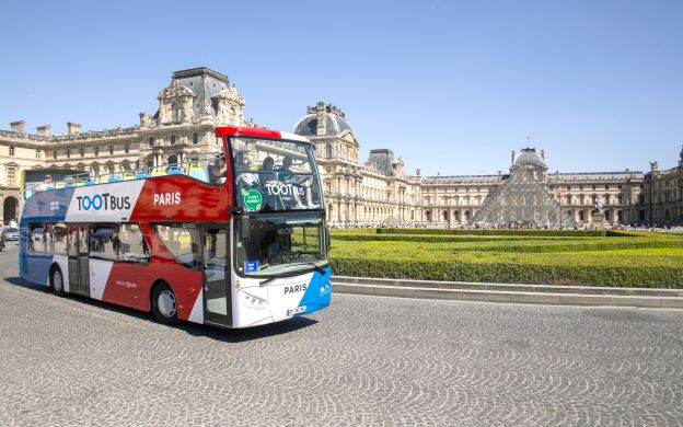 Toot bus Paris with majestic backdrop of Grand Louvre Museum: A captivating blend of modern transportation and cultural heritage.