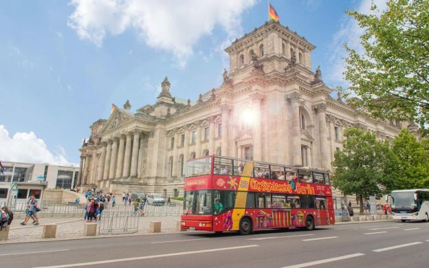 A vibrant hop-on, hop-off bus moves through the streets of Berlin, offering tourists an immersive experience of the city's bustling atmosphere.