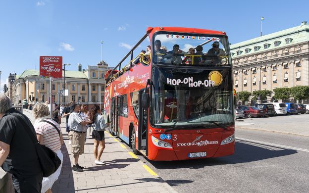 Passengers eagerly await to hop on the Red Sightseeing Stockholm, their expressions filled with anticipation for the open tour bus adventure.