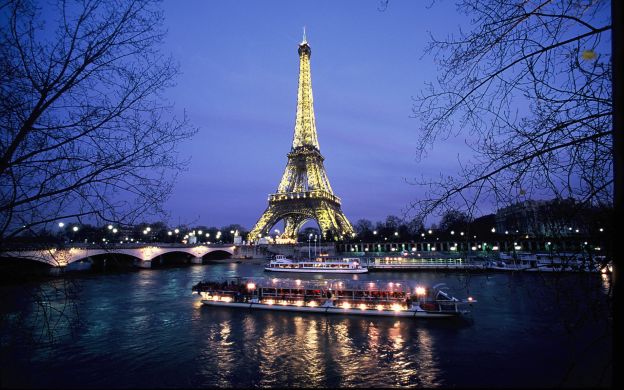 Captivating view of cruise ships gliding along the beautiful river, framed by the illuminated Eiffel Tower in all its nighttime splendor.