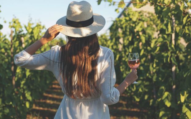 A girl poses stylishly, holding a wine glass behind her back, exuding elegance and sophistication in the photograph.