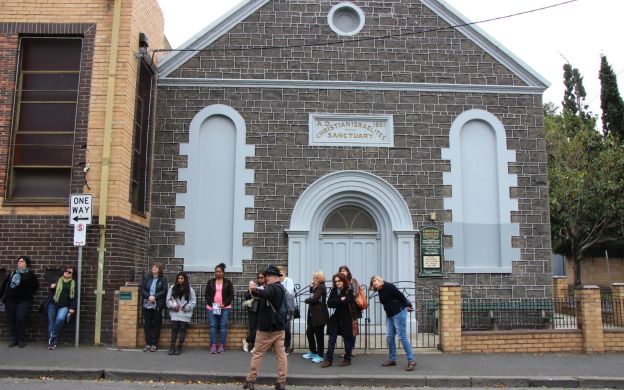 A group of tourists poses for a photo outside the Christian Israelite Church in Melbourne, capturing a memorable moment together.