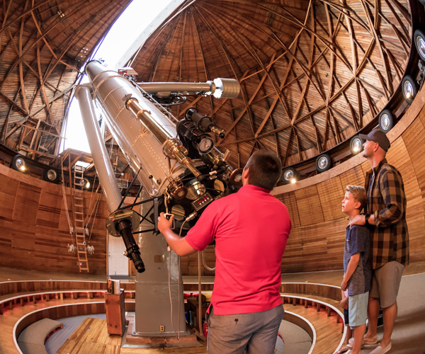 Two men and a boy look through a giant telescope at the sky