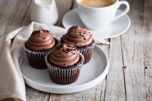 Chocolate cupcakes on a platter with latte in background