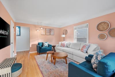 Cozy living room with a gray sectional sofa, blue armchair, wooden coffee tables, and peach walls decorated with woven art.