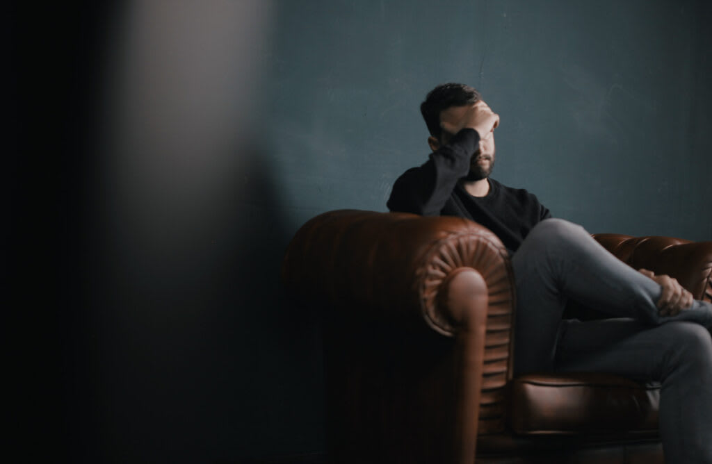 A man sitting alone in thought on a leather sofa