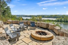 A peaceful outdoor fire pit area with chairs overlooking a river and forest.