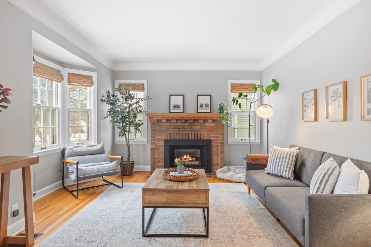 A cozy living room featuring a gray sofa, a brick fireplace, and ample natural light.