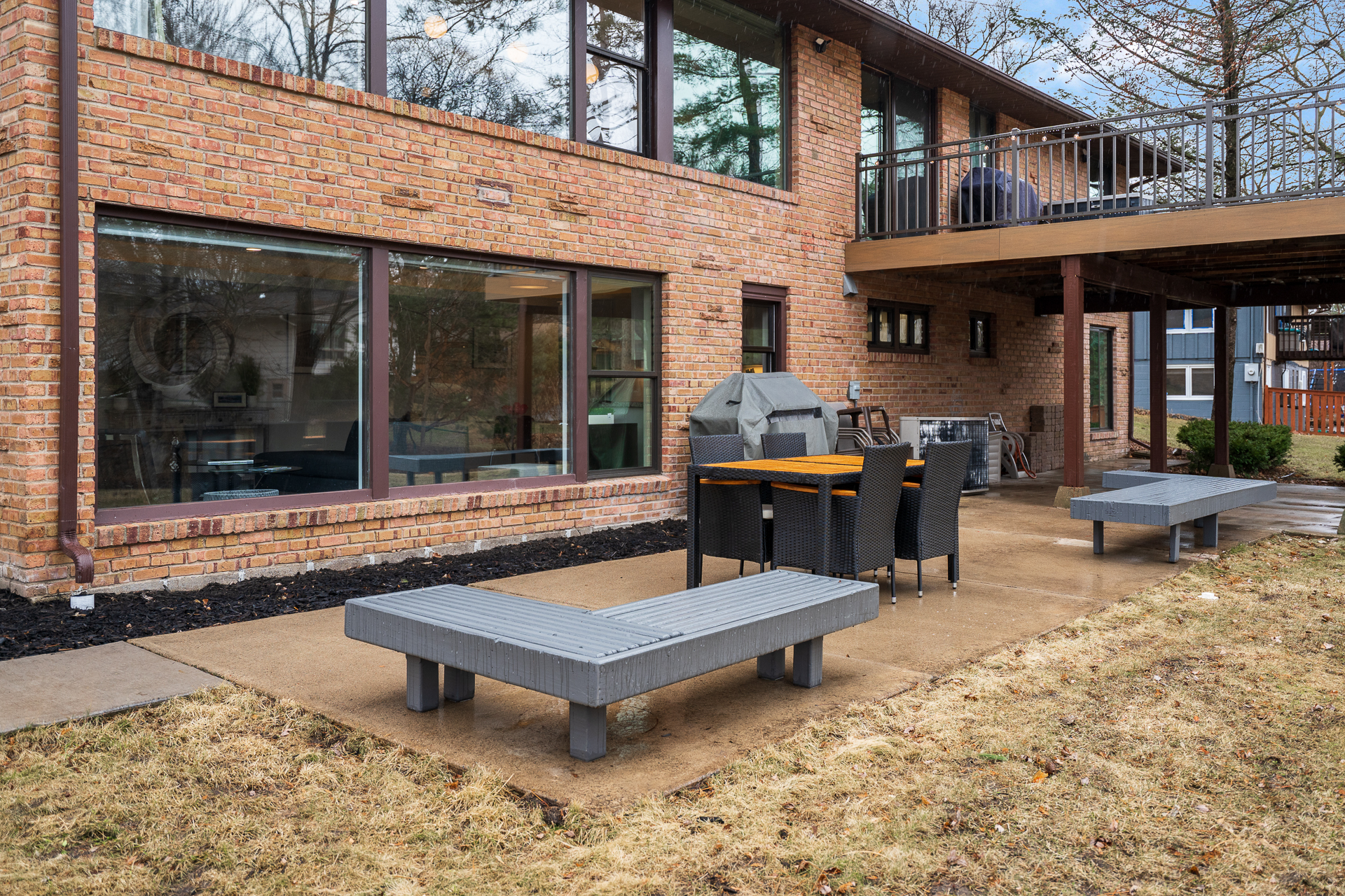 A modern outdoor seating area next to a brick house, featuring a dining table and grill.