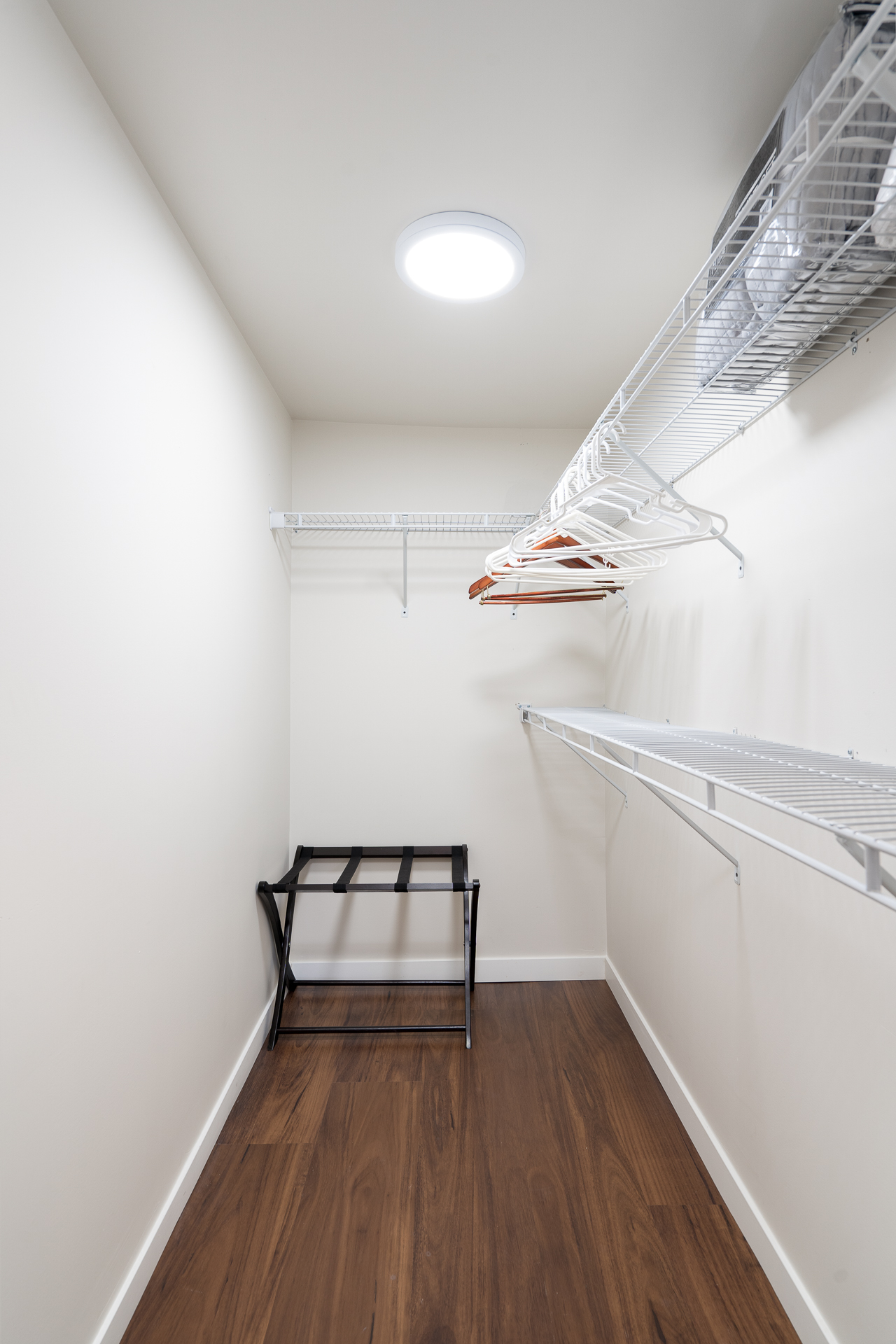 A minimalistic closet featuring wire shelves and a folding stool.