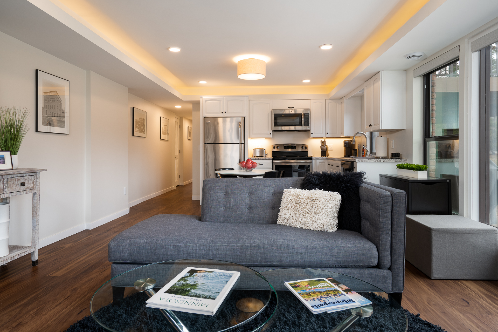 A modern living area featuring a stylish grey sofa and an open kitchen.