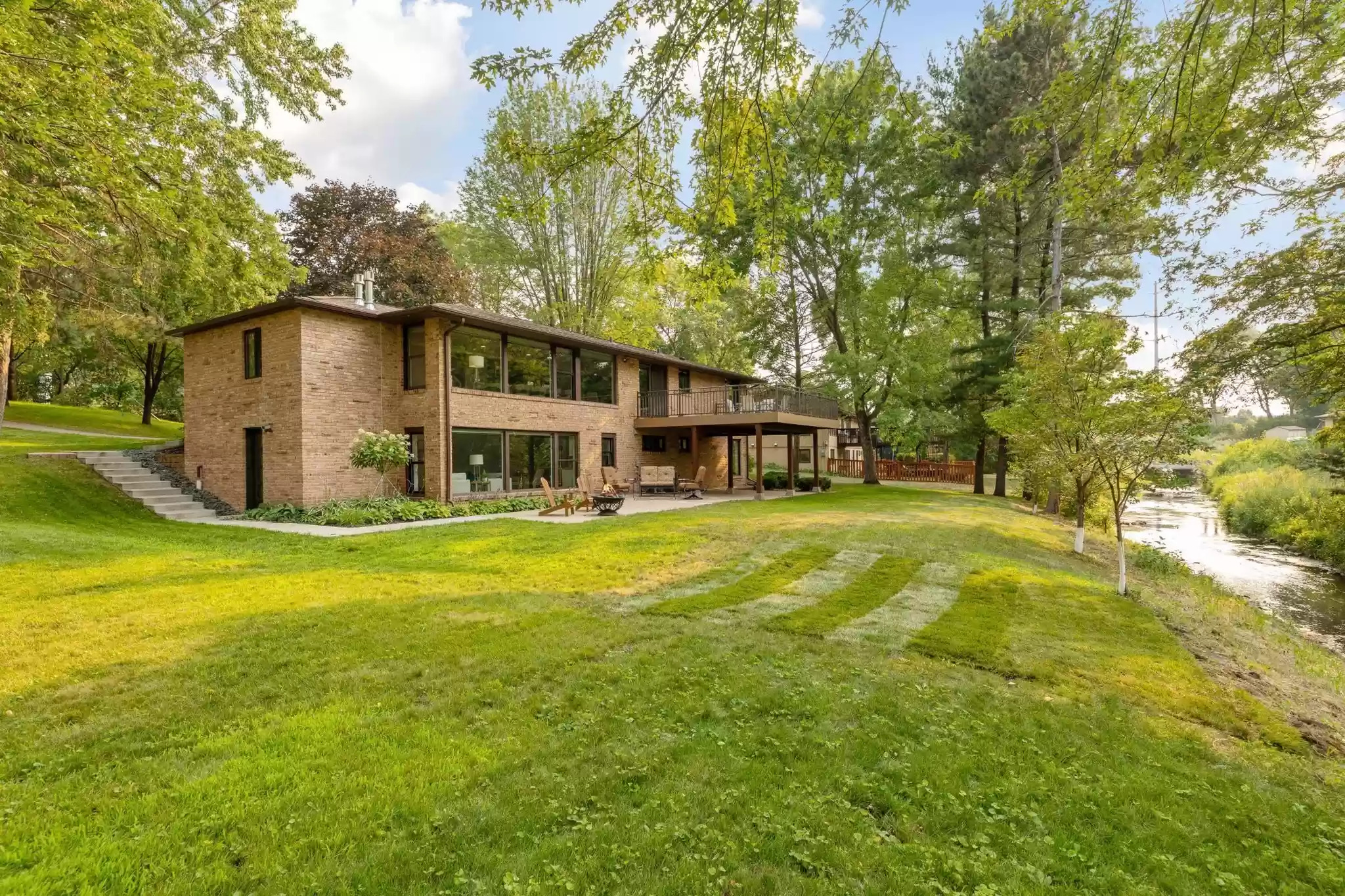 A modern brick house surrounded by lush greenery and a serene creek.