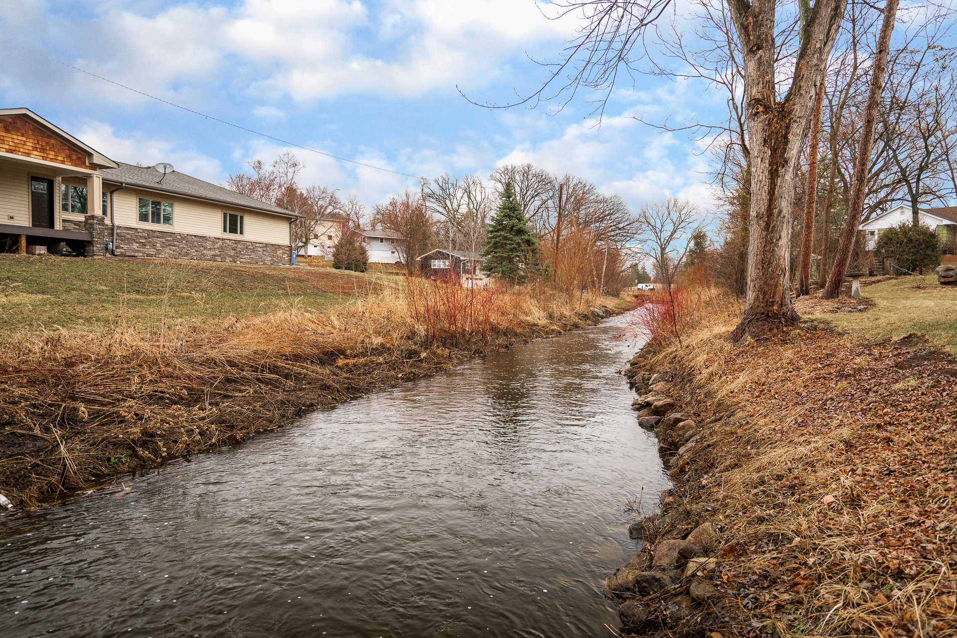 A serene stream bordered by homes and nature in a suburban setting.