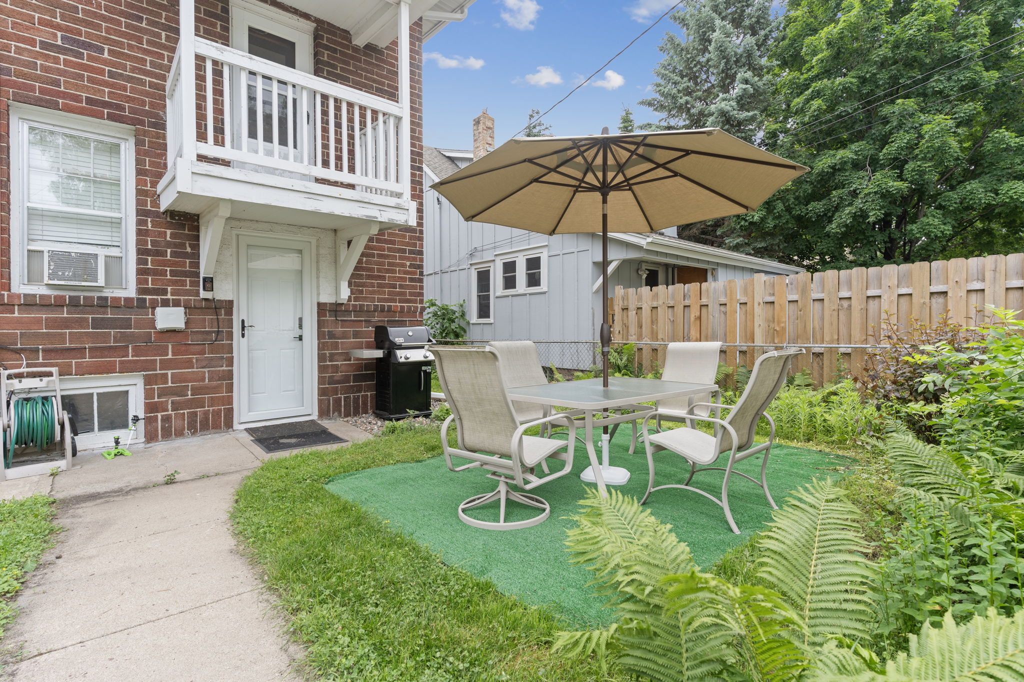 A charming outdoor patio with a dining set and grill next to a brick building.