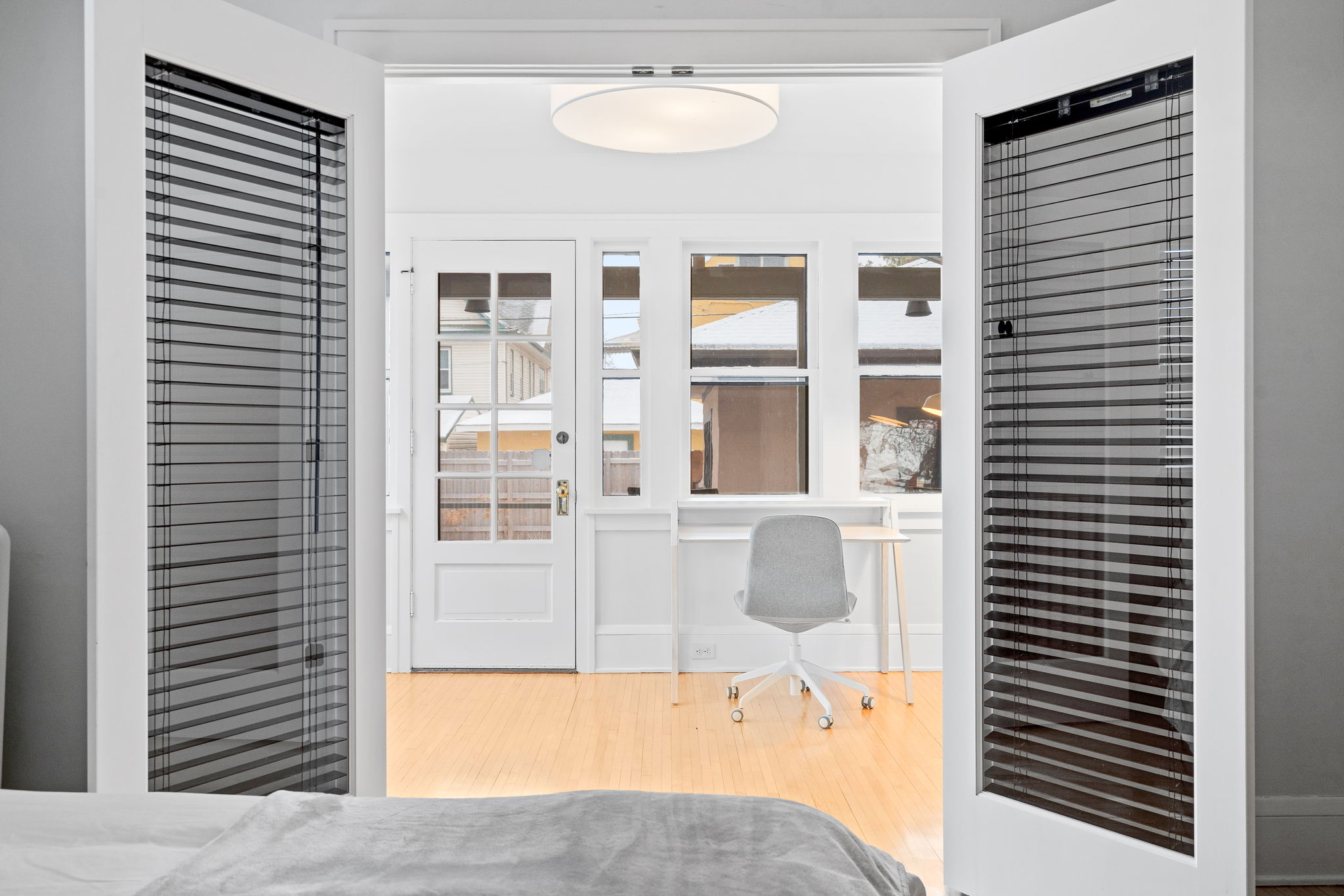 A tranquil view from a bedroom into a well-lit workspace beyond the double doors.
