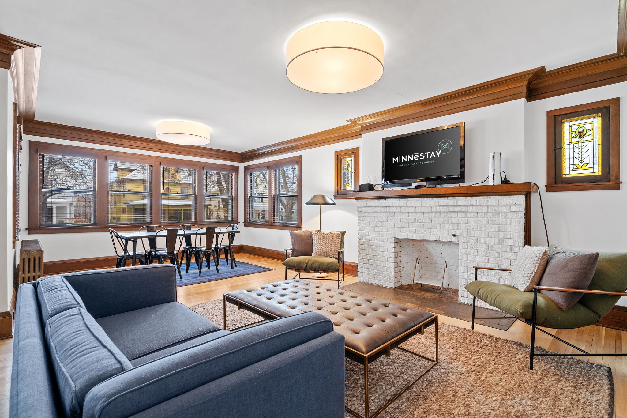 Cozy living room featuring a blue sofa, tufted coffee table, and large windows with wooden trim.