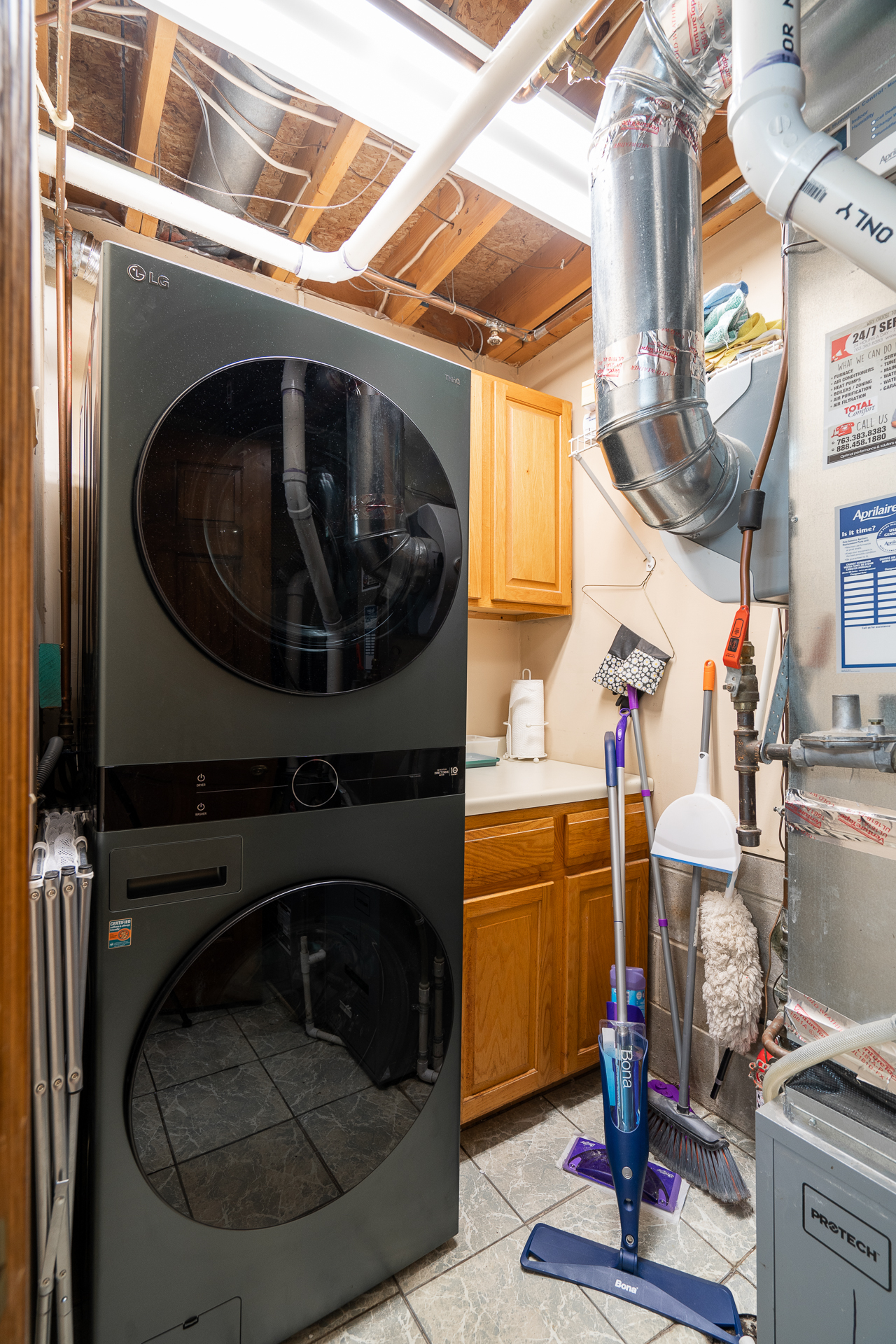 A modern laundry room with a stacked LG washer and dryer, complemented by wooden cabinets and cleaning supplies.