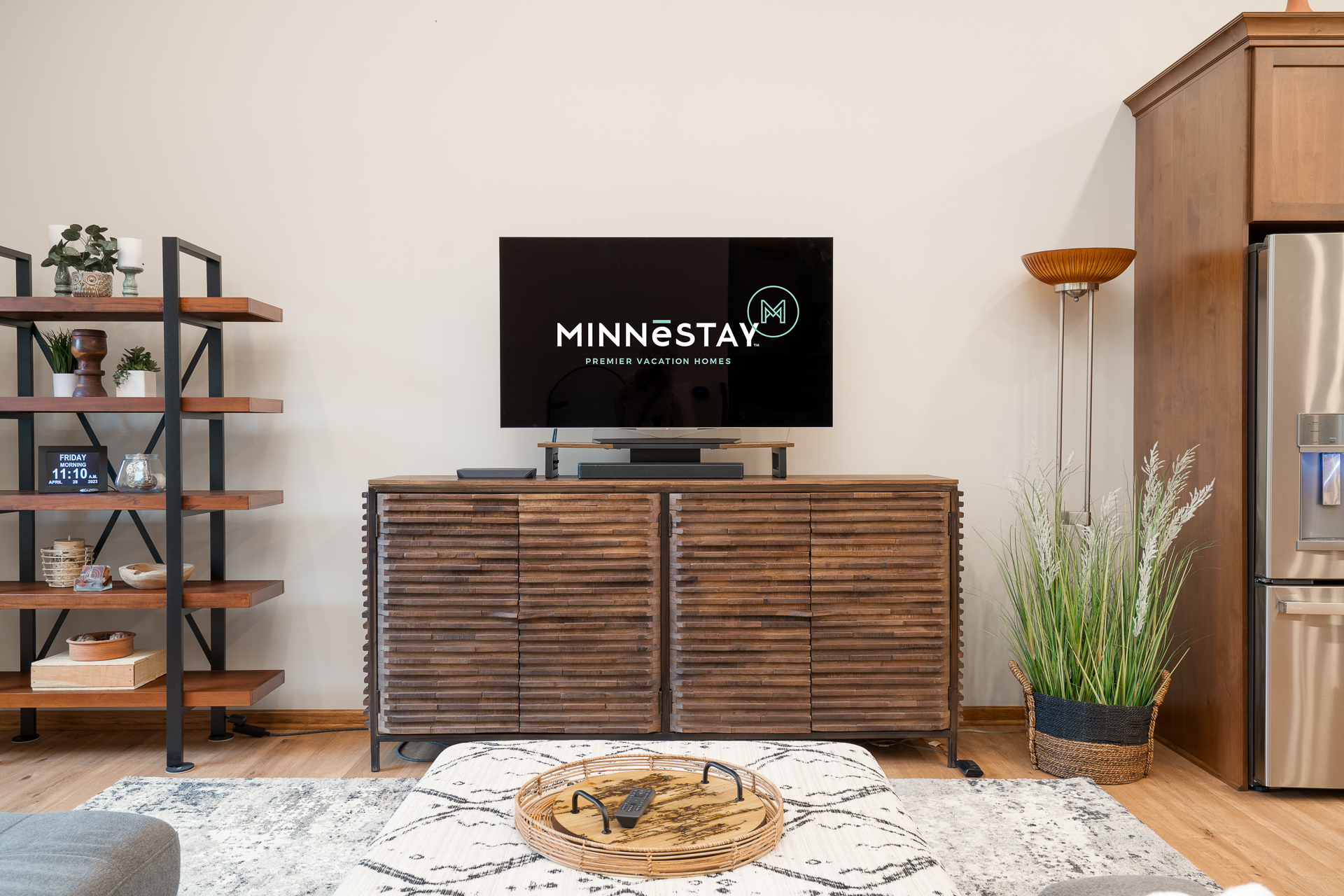A modern living space featuring a slatted media console, a television displaying a logo, and stylish decor.
