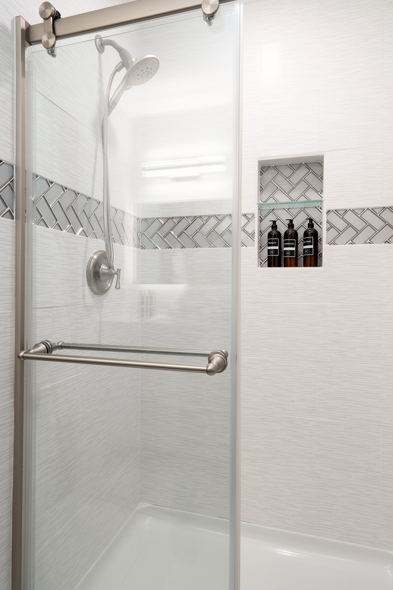 Stylish modern shower with glass enclosure and herringbone tile accents.