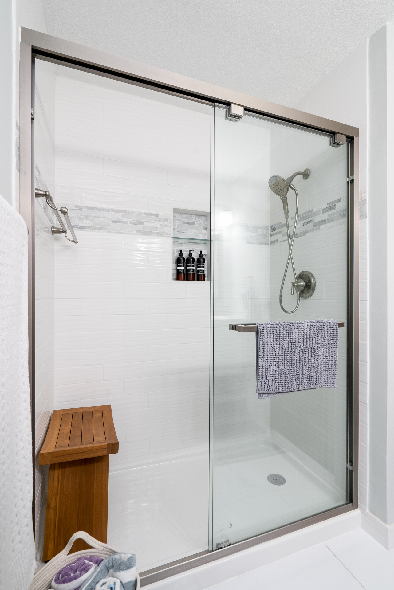 A tranquil modern shower enclosure with glass doors and a wooden bench.