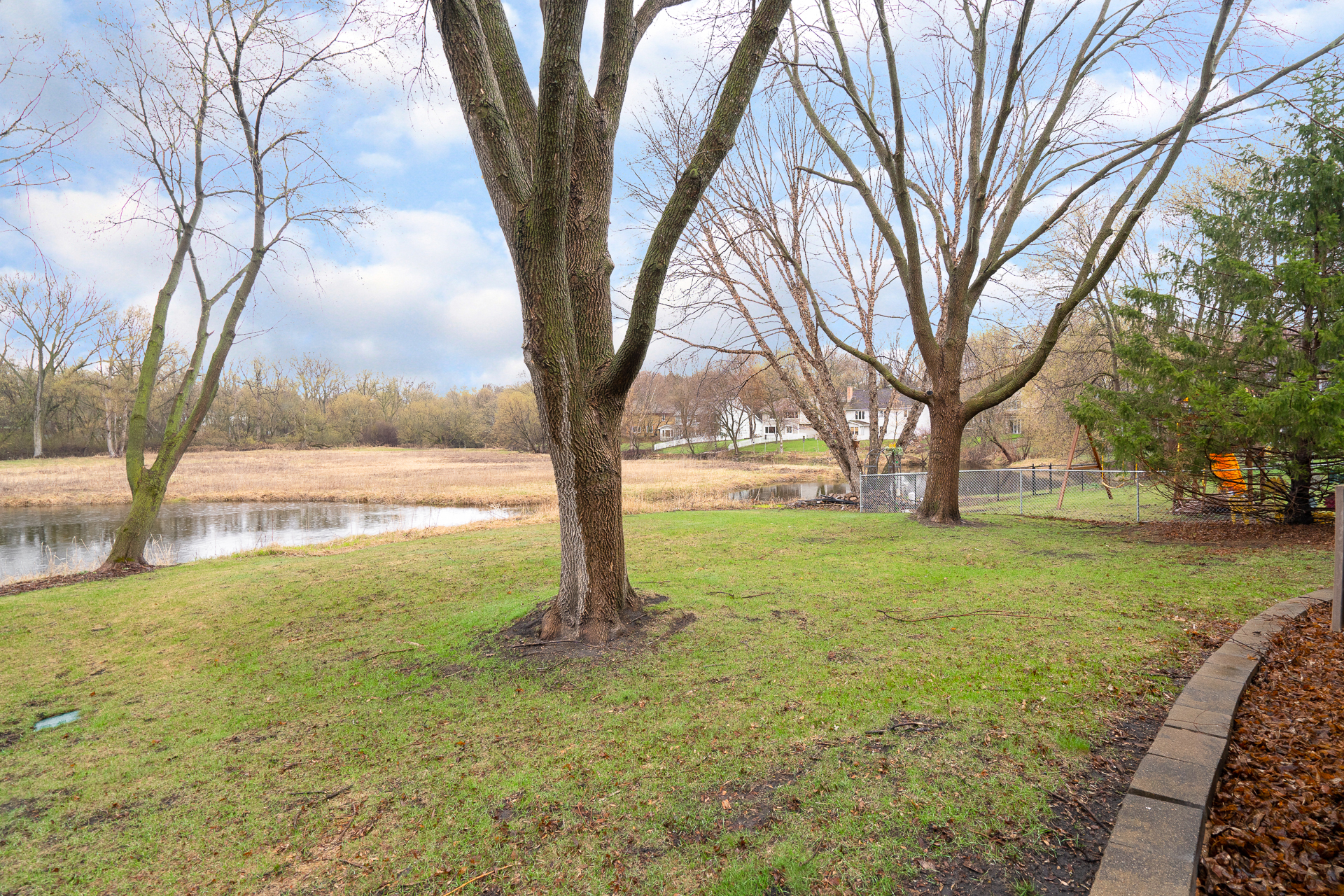 A tranquil pond view with trees and a distant house in early spring.