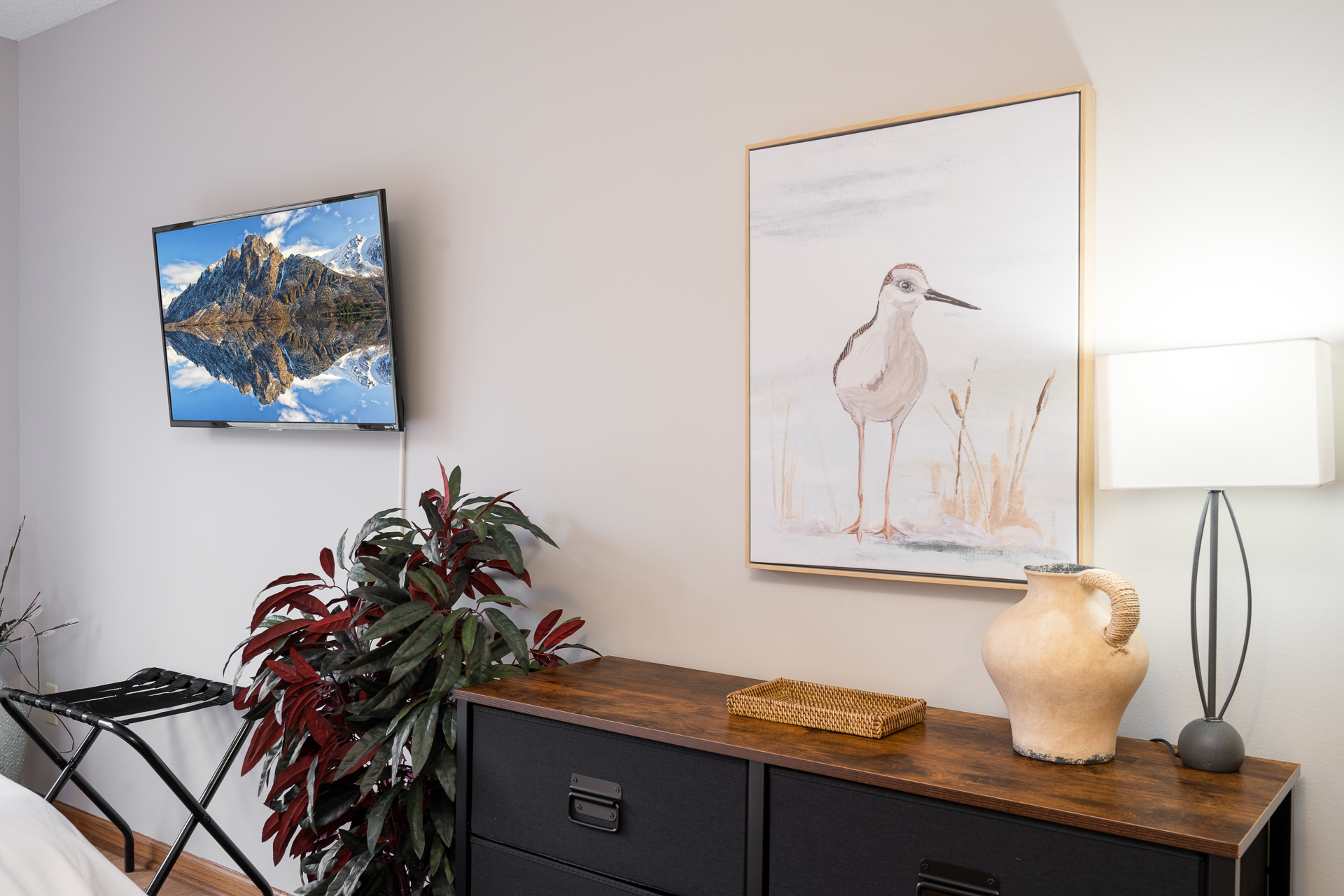 A cozy room corner with modern decor featuring art, a TV showing a mountain landscape, and a stylish lamp.