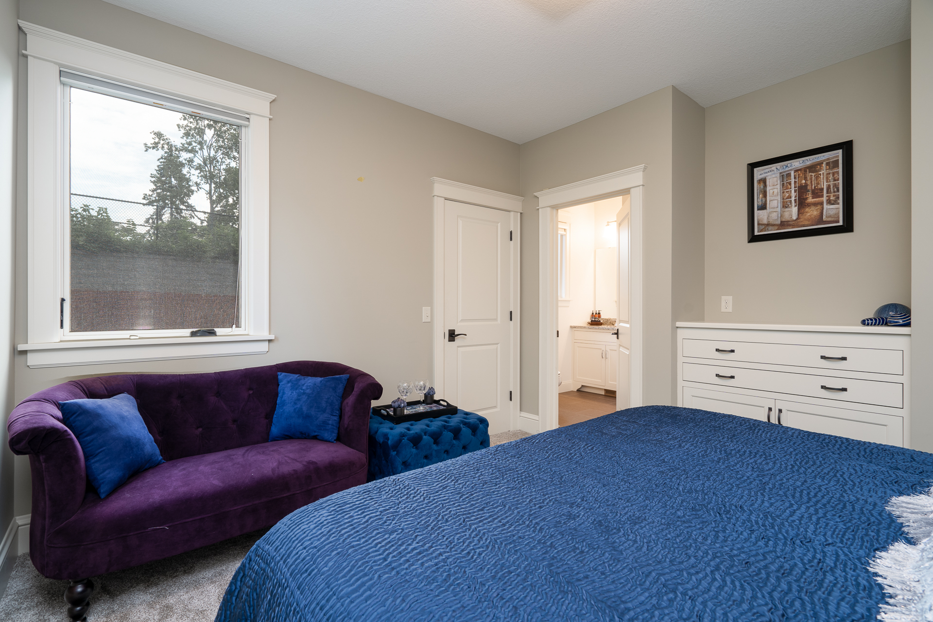 A stylish modern bedroom featuring a plush blue bedspread and a cozy purple loveseat.